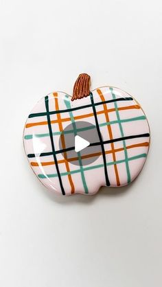 an orange and green ceramic apple with a tassel on it's end, sitting on a white surface