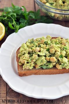 an avocado toast on a white plate next to lemons and parsley