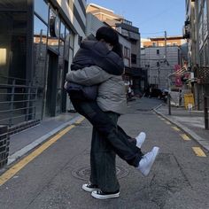 two people hugging each other in the middle of an empty street with buildings behind them