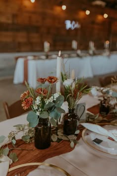 the table is set with candles, plates and vases filled with flowers on it