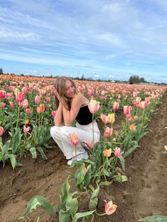 a woman kneeling down in the middle of a field with pink and yellow tulips