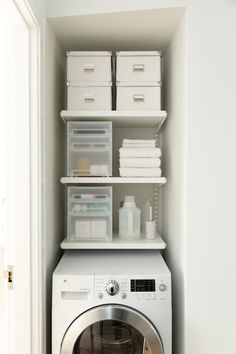 a washer and dryer in a small room with white shelves on the wall