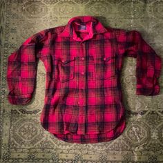 a red and black plaid shirt laying on top of a rug next to a wall