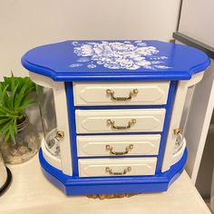 a blue and white table with drawers next to a potted plant on a counter