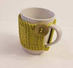 a knitted coffee cup cozy with a button in the middle and a yellow handle