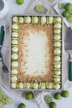 a square cake with limes around it on a white table cloth next to utensils