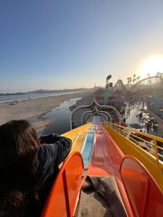 people are riding on a roller coaster at an amusement park near the water's edge