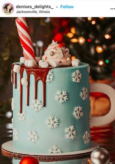 a blue cake with white snowflakes and candy canes on top, sitting in front of a christmas tree