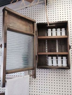 an open wooden box with white jars in it hanging on the wall next to a towel rack