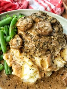 a white plate topped with mashed potatoes covered in mushroom gravy and green beans