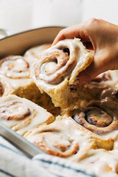 a person holding a piece of cinnamon roll in a pan with icing on top