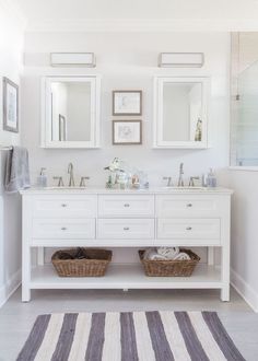 a white bathroom with two sinks, mirrors and baskets on the counter top in front of it