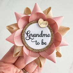 a hand holding a pink and gold pin with the words grandma to be on it