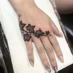 a woman's hand with black leaves and vines tattooed on the middle of it