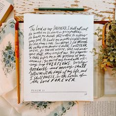 an open book with writing on it next to a pen and flower pot filled with flowers