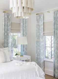 a white bed sitting in a bedroom next to two windows with blue drapes on them