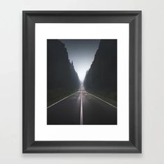 a black and white photo of an empty road in the middle of mountains with trees on both sides