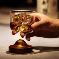 a hand holding a glass with some liquid in it and ice cubes on the rim