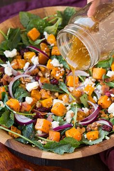 someone pouring dressing onto a salad in a wooden bowl