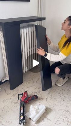 a woman kneeling on the floor next to a radiator holding up a piece of furniture