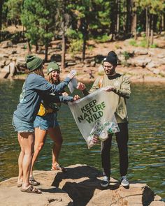 three people standing on the edge of a body of water holding a sign that reads keep nature wild