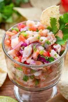 a glass bowl filled with shrimp salad and tortilla chips next to lime wedges