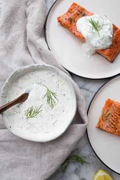 two plates with salmon and cream sauce on them next to a bowl of sour cream