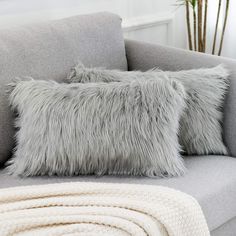 two gray pillows sitting on top of a grey couch next to a white throw pillow