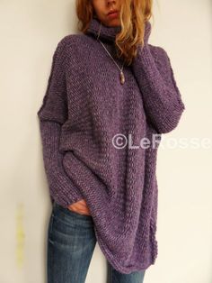 a woman wearing a purple sweater leaning against a white wall with her hands on her hips