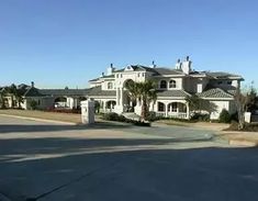 a large white house sitting on the side of a road with palm trees in front of it