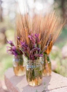 three mason jars filled with dried flowers on top of a stone slab in the grass