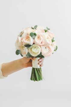 a hand holding a bouquet of white and pink flowers with greenery on the stems