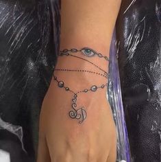 a woman's hand with an evil eye and chain tattoo on her left wrist