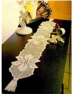 a table runner with white crocheted lace on it next to a vase filled with flowers