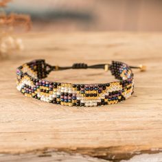 a close up of a beaded bracelet on a wooden table with flowers in the background