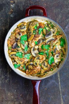 a pan filled with mushrooms and greens on top of a wooden table next to a red spatula