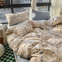 an unmade bed sitting in front of a window next to a checkered floor