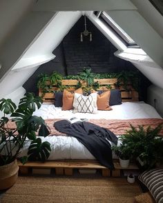 a bed with pillows and blankets in an attic bedroom, surrounded by potted plants