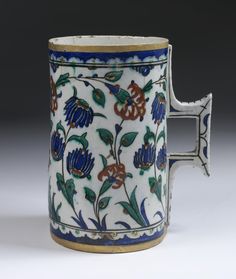 an ornately decorated coffee cup with blue and red flowers on the outside, sitting on a white surface