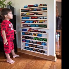 a young boy standing in front of a toy train set on a wall mounted shelf