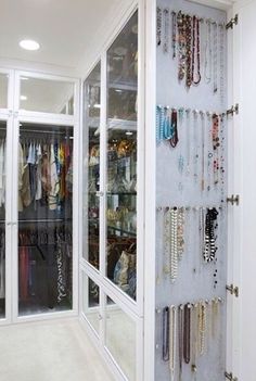 a closet filled with lots of necklaces and bracelets hanging on the wall next to glass doors