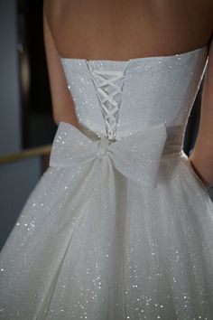 the back of a white wedding dress with sequins on it and a bow at the waist