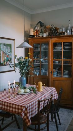 a dining room table set for two with flowers and candles on it in front of a china cabinet