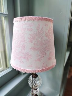 a pink lamp sitting on top of a table next to a window