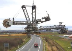 a large crane sitting on the side of a road next to a lush green field