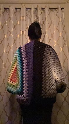 a woman standing in front of a curtain with a crocheted jacket over her shoulders