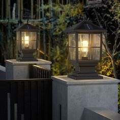 two lamps on top of cement pillars with trees in the background