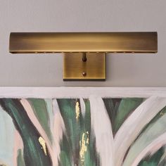 a painting is hanging on the wall next to a light fixture with a gold finish