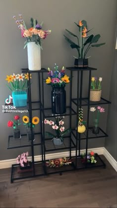 a black shelf filled with vases and flowers on top of each other next to a wall