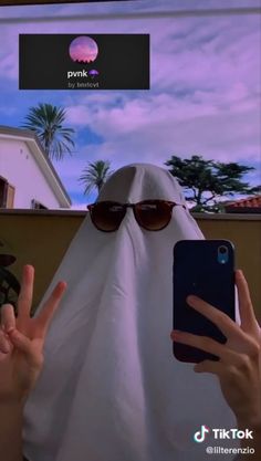 a person in a white burka holding up two fingers to take a photo with their cell phone